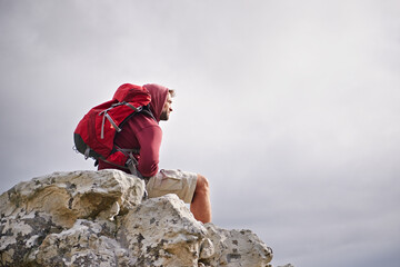 Man, mountain and think on nature hike for calm, cliff and peace or inspiration on rocks for wellness. Person, exercise and travel with backpack on vacation, adventure and relax on cliff for health