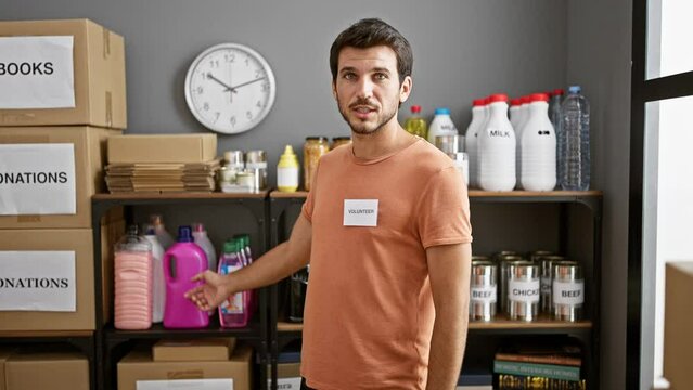 A young hispanic man volunteers at a food donation center, organizing shelves stocked with groceries in an indoor setting.