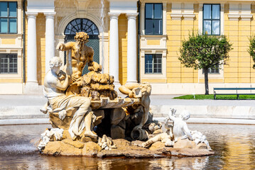The Ehrenhofbrunnen fountain at Schonbrunn Palace stands under a clear blue sky, with water...