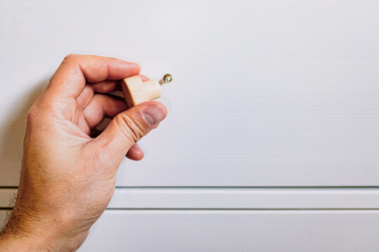 A person's hand installing a simple wooden knob on the door of a white cabinet, representing home improvements.