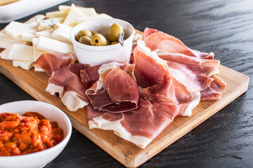 Charcuterie board, sophisticated appetizer setting. Meat and cheese board with a variety of cheeses and slices of cured meats.