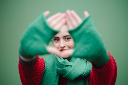 Woman looking through finger frame against green background