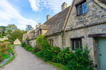 Fototapeta na wymiar Scenic view of traditional old cottage houses and a street by a river in a beautiful English village, Bibury village in the Cotswolds Area of Outstanding Natural Beauty in Cirencester, England.