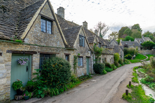 Scenic view of traditional old cottage houses and a street by a river in a beautiful English village, Bibury village in the Cotswolds Area of Outstanding Natural Beauty in Cirencester, England.