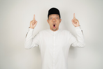 Wow face shocked expression Asian Muslim man wearing Arab costume pointing hand finger at empty space on isolated background - obrazy, fototapety, plakaty