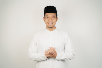 Happy smiling Asian Muslim man in Arabic costume standing with Eid greeting gesture and welcoming Ramadan isolated background - obrazy, fototapety, plakaty