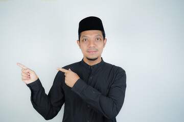 Cheerful handsome Asian Muslim man pointing hand finger at empty space for advertising on isolated background - obrazy, fototapety, plakaty