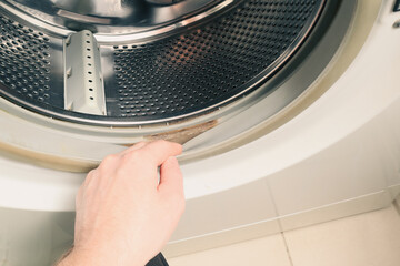 Dirty moldy washing machine sealing rubber. The person checks the dirt on the rubber of a washing machine. Cropped hand holding washing machine.