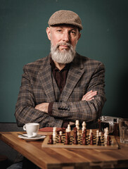 Portrait d'un homme quinqua hipster en costume assis à une table avec un appareil photo argentique, un café et un jeux d'échec qui regarde droit devant lui