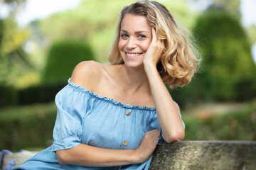 happy blonde woman sitting outdoor and thinking - obrazy, fototapety, plakaty