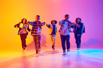 Portrait of youth dance group strides forward in sync in neon light against gradient colorful...