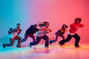 Casually dressed teenagers perform forward-moving dance sequence in neon light against gradient studio background. Concept of hobby, sport, fashion and style, action, youth culture, music and dance.