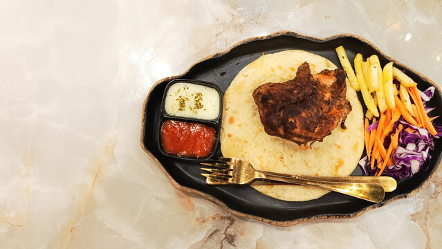 landscape of dajaj mashwi, oven roasted chicken (ayam panggang oven) served with 2 khubus (pita bread), french fries, salata, chili sauce and thum with empty space on the side
