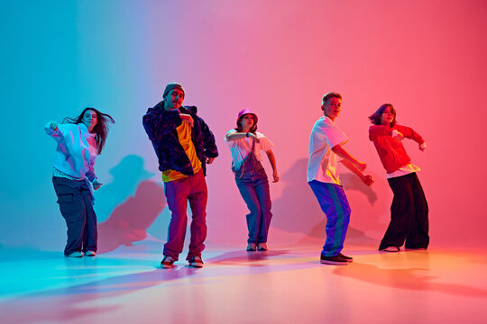 Modern dance crew in synch motion performing hip-hop in neon light against gradient colorful studio background. Concept of hobby, sport, fashion and style, action, youth culture, music and dance.