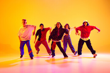 Urban dance crew in casual outfits in mid-dance in neon light against gradient colorful studio...