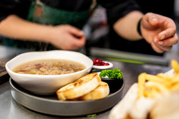 A chef meticulously prepares a meal, featuring a bowl of soup, grilled bread, and artful...