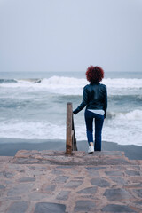 Young curly woman with red hair in casual clothes walk down stairs to a beach at a rainy day