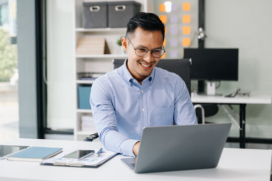 Asian man using laptop and tablet while sitting at her working place. Concentrated at work.
