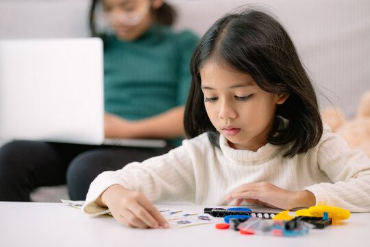 A young girl is sitting at a table with a laptop and a stack of Legos