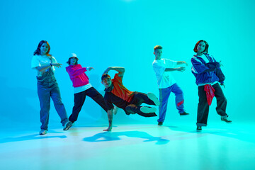 Group of young hip-hop dancers energetically moves in sync in neon light against gradient colorful...
