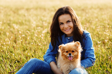 girl in the field. cheerful girl in black hair and a blue shirt sits in a field with a small fluffy dog, nature concept