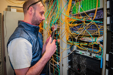 A man holds a broken wire in his hands. A technician is trying to fix a breakdown on a trunk line in a data center server room.