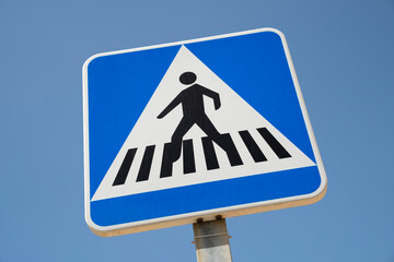 Low angle view of a Spanish pedestrian zebra crossing road sign, against the background of a clear blue sky.