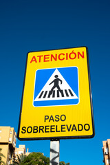 Low angle view of Spanish pedestrian zebra crossing road sign, against a clear blue sky.