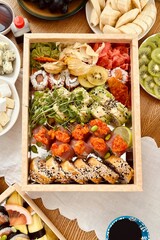 a set of sushi. rolls decorated with green beans, kiwi slices, physalis, corn chips, micro greens next to ginger and wasabi. order. delivery to the customer. view from above
