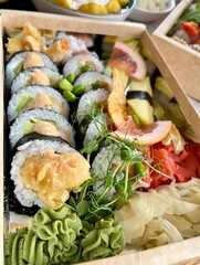A set of sushi is close. rolls decorated with green beans, a slice of grapefruit, corn chips, micro-greens next to ginger and wasabi. order. delivery. side view