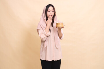 Asian Muslim woman is shocked to see dimsum and holds a wooden bowl in front of her chest containing delicious dimsum