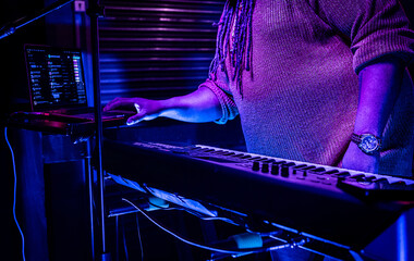 Keyboard synth artist with laptop giving a club performance in a neon purple ambiance