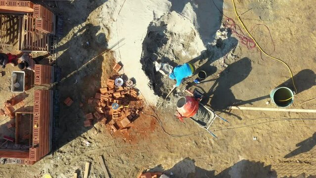 Above top view on building site area, construction worker is using shovel to fill up mixer as making concrete, mortar.
