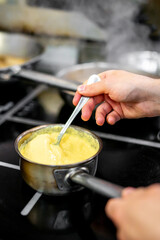 A person stirs a creamy mixture in a saucepan on a stove, capturing the warmth and diligence of...