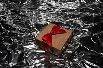 A box with a red bow lies on a silver background. Stylish photo of a box with a surprise.