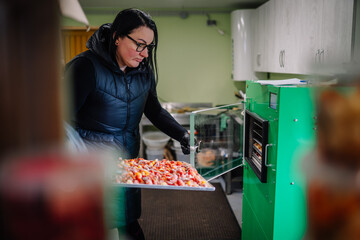 A woman in a black vest is carefully placing a tray of frozen tomatoes into a large green...