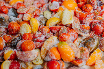 Heap of halved, frosty tomatoes with ice crystals, in a mix of red and yellow colors.