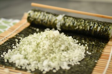 rice spreading on a nori sheet with a bamboo mat