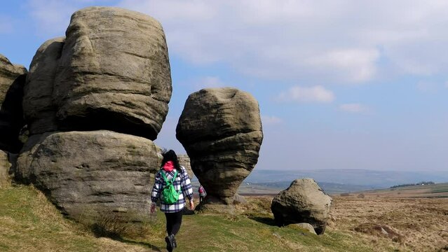 Rear view of woman walking past weather sculptured Bride Stone boulders in North West of England, UK.