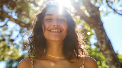 Smiling woman with sunlit hair standing under a tree with a radiant sky in the background.
