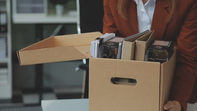 Upset female employee packing belongings in box, frustrated stressed girl getting fired from job ready to leave on last day at work. sad office worker desperate from work