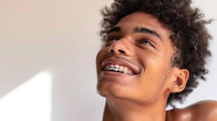 A young man with curly hair wearing braces smiling and looking up with a joyful expression.