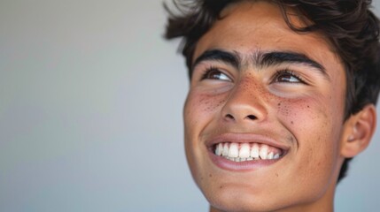 A young man with a radiant smile freckles and dark hair looking upwards with a joyful expression. - obrazy, fototapety, plakaty