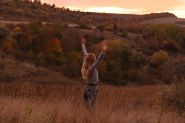Young attractive blonde woman standing on the hill at sunset