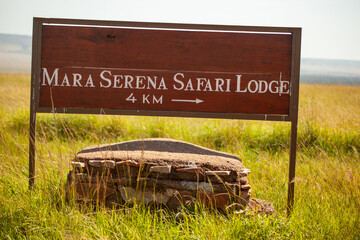 A sign for Mara Serena Safari Lodge is sitting on a rock in a field
