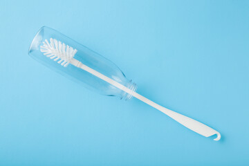White washing brush inside transparent plastic bottle on light blue table background. Pastel color. Closeup. Top down view.