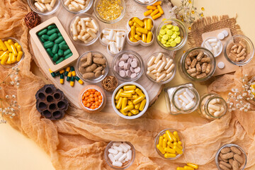 Big amount of various dietary supplements pills, vitamins, minerals, tablets and capsules in small jars from above on a wooden desk on beige background in rustic style.