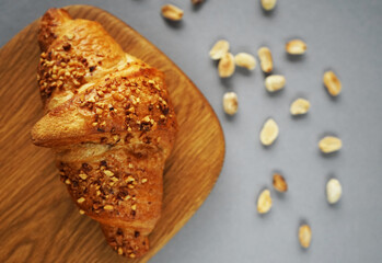 Croissant with peanut crumbs and cream on a wooden board next to scattered peanuts