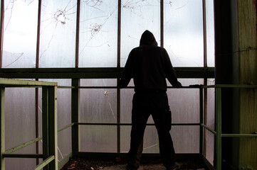 A mysterious hooded, figure, back to camera, standing in a abandoned industrial building - obrazy, fototapety, plakaty