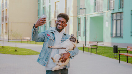 African american man with positive facial expression taking selfie photo with pug dog during walk....
